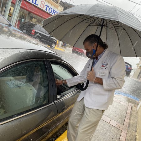 Pharmacist Francisco Javier Jiménez Ramírez interacting with a patient in front of his parent’s pharmacy on a rainy day in Lares, Puerto Rico.