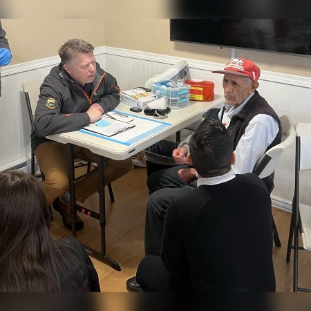 With the help of a Spanish-speaking interpreter, Kevin Cleveland, PharmD, listens to the health concerns of an older Mexican American patient at a pop-up vaccine clinic for immigrants and migrant workers in Caldwell, Idaho.