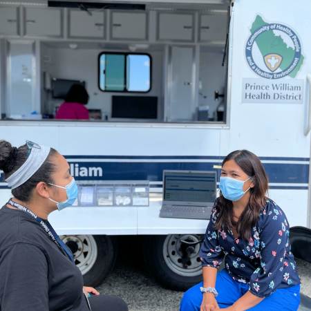 Pharmacist Precious Hoffmann (right) talks to a colleague in front of the Virginia Department of Health mobile clinic for the Prince William Health District.