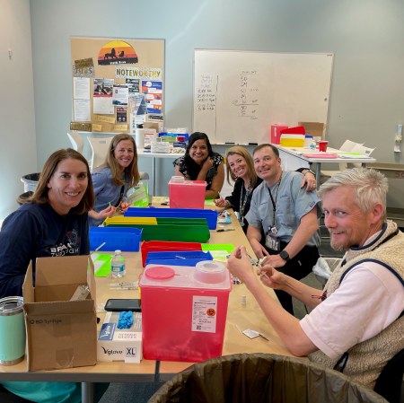 Pharmacist Toral Patel (seated at head of table) along with other faculty from University of Colorado Skaggs School of Pharmacy and Pharmaceutical Sciences drawing up vaccine doses for COVID-19 vaccination clinics hosted by the University of Colorado Anschutz Medical Campus.