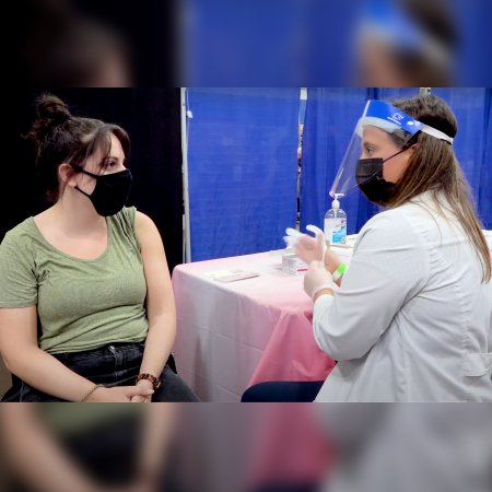 Student pharmacist Victoria Fusco dons gloves before vaccinating a community member during a pop-up vaccine clinic in the gym at Notre Dame of Maryland University.